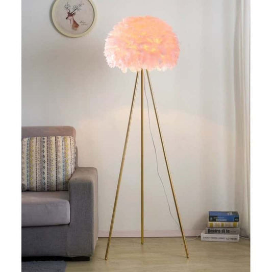 Lampadarul trepied cu abajur din pene roz, aprins, lângă o canapea gri și câteva cărți
